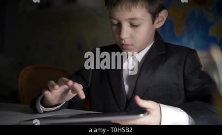 boy in jacket using tablet, doing homework at home, playing at the game Stock Photo