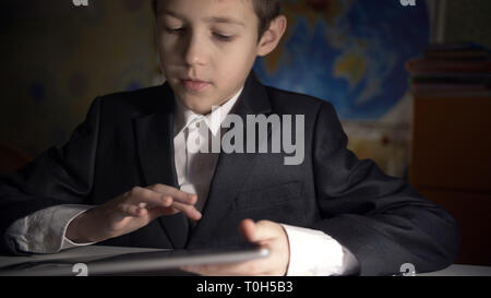 boy in jacket using tablet, doing homework at home, playing at the game Stock Photo