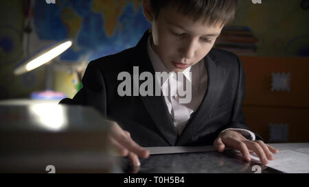 boy in jacket using tablet, doing homework at home, playing at the game Stock Photo