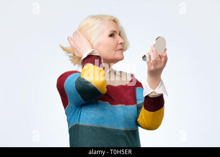 Smiling senior blond woman with mirror over white background Stock Photo