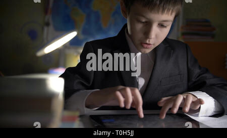 boy in jacket using tablet, doing homework at home, playing at the game Stock Photo