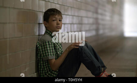 sad lonely battered boy sits on the floor in a tunnel in deep depression looking at the camera, no one is waiting for the boy at home Stock Photo