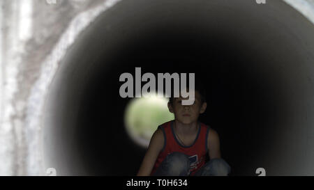 Sad upset abused teenager boy sitting alone hiding inside of a drainage tunnel, pain on face, broken life, regret, refugee