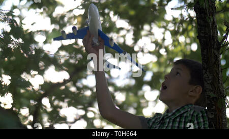 dreamer boy sitting on tree and playing with toy airplane Stock Photo