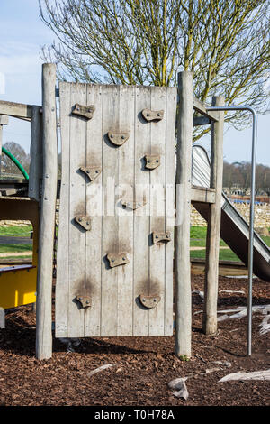 A childrens wooden climbing wall with large easy hand and footholds in a childs playground area Stock Photo