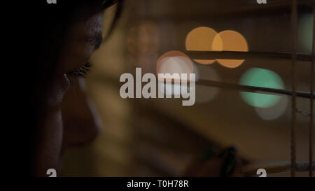 young brunette with brown eyes peeks through the window with her finger, pushing open the blinds Stock Photo