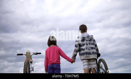 boy with girl standing with bicycles on the top and holding hands in the field Stock Photo