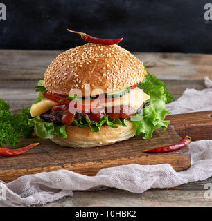 fresh homemade burger with lettuce, cheese, onion and tomato on a rustic wooden board, close up Stock Photo