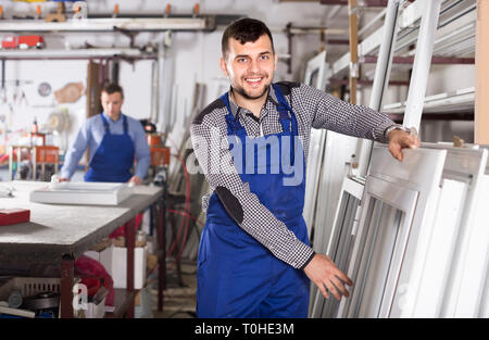 Young laborer is inspecting the window frame in workshop. Stock Photo