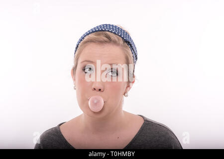 Pretty young blond woman with big, bright eyes, wearing a cute retro outfit, blowing pink bubble gum.