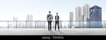 Rear view of two asian business people standing on modern terrace and looking at view on the city Stock Photo