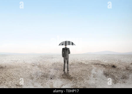 Rear view of asian businessman standing with black umbrella on the dry land over blue sky background. Earth day concept Stock Photo