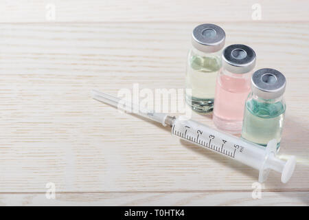 Vaccine vials and syringe on white wooden background. Various color and type of medications. Healthcare and vaccination. Stock Photo