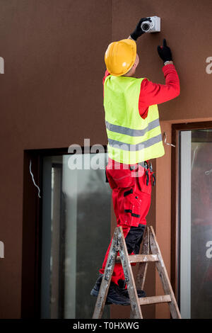 Technician worker installing video surveillance camera on wall Stock Photo