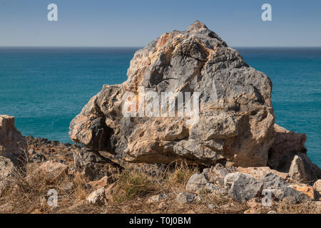 Colorful big rock on the edge of a hill at the seaside. Calm water of the Mediterranean sea and its horizon in the background. Clear blue sky. Herakli Stock Photo