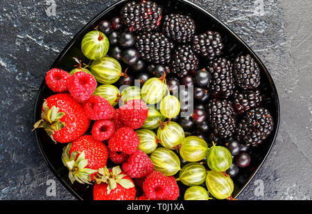 Photo on top of blackberries, strawberries, raspberries, gooseberries,black currant on black plate Stock Photo