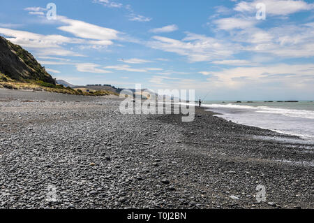 Lone angler fishing. Black sand beach on the east coast of the South Island of New Zealand in the Canterbury region. Pacific ocean coast Stock Photo