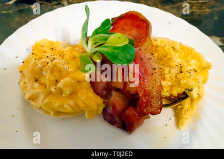 Breakfast snack in Yorkshire a toasted muffin with two slices of fried bacon and scrambled egg Stock Photo