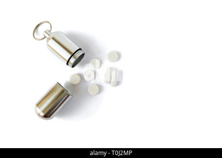 Silver medicine bottle with white pills next to it, isolated on white background. Portable key chain container for pills and small items, useful for h Stock Photo