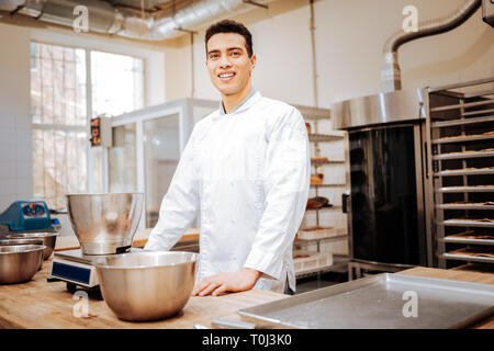Dark-haired chef wearing white uniform standing in the kitchen