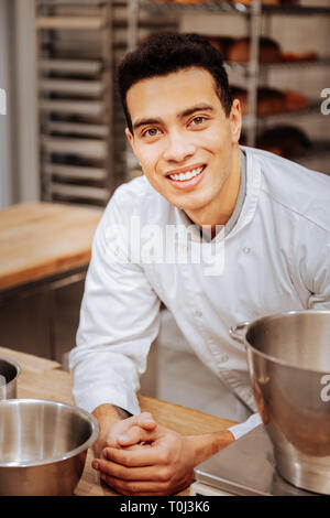 Dark-haired cheerful baker feeling excited before starting work Stock Photo