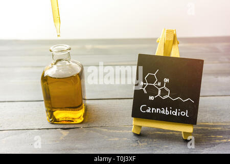 Cbd oil in glass bottle and chalkboard with molecule drawing on wooden table Stock Photo