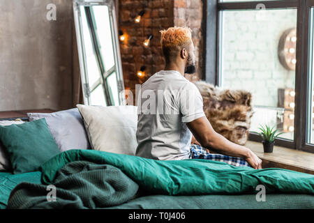 Nice pleasant man sitting on the bed Stock Photo