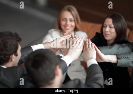 Group of happy business people holding hands together while sitting around the desk Stock Photo