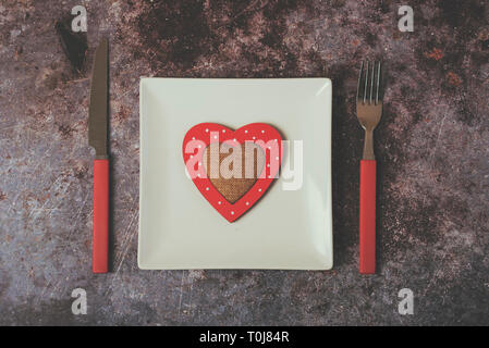 red heart on a white plate next to cutlery against Grunge background Stock Photo