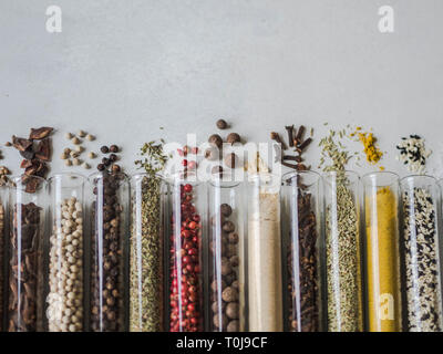 Various dry spices in glass tubes and spilled on gray background. Stock Photo