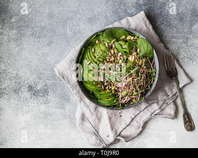 Green healthy salad of spinach, sprouts, avocados and various seeds in a blue bowl Stock Photo