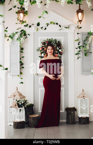 Charming pregnant woman in marsala dress posing on steps of house. Stock Photo