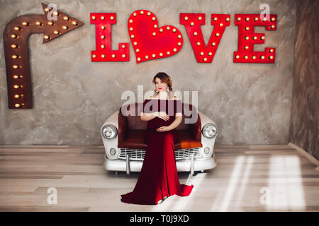Charming pregnant woman in marsala dress posing on steps of house. Stock Photo