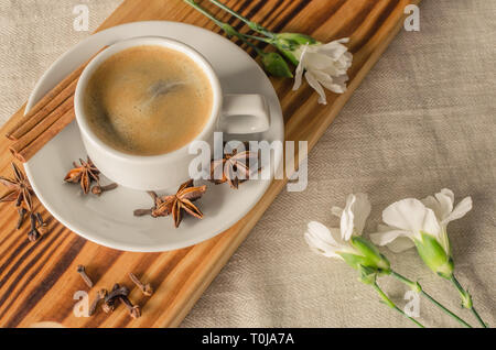 A cup of espresso, cinnamon sticks, anis stars and white carnations on wooden desk and textile background. Good morning! Stock Photo