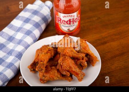 ATLANTA, GEORGIA - April 19, 2017:  Buffalo Chicken Wings on a white plate with a bottle of Frank's Red Hot Sauce in background Stock Photo
