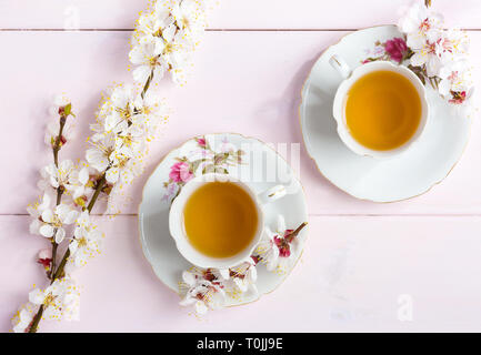 Two cups of tea and spring flowers (blooms of an Apricot) on a light pink wooden table. Stock Photo