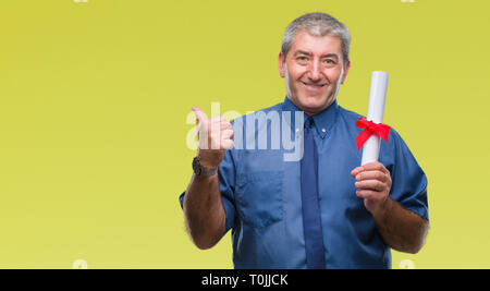 Handsome senior man holding degree over isolated background pointing and showing with thumb up to the side with happy face smiling Stock Photo