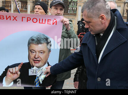 Kiev, Kiev, Ukraine. 20th Mar, 2019. An activist of the ''Movement of New Force party, of former Georgian President Mikhael Saakashvili, is seen holding fake dollar bills in front of a banner with a photo of Ukrainian President Petro Poroshenko outside the Presidential office during the protest.The activists protest against alleged corruption in the country's defence industry, and demand an investigation and arrests of the top figures in an alleged military corruption scandal, which they were accused of profiting from the sales of state defence companies at inflated prices of smuggled Russi Stock Photo