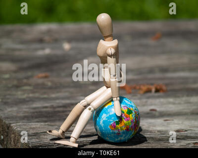 A wooden mannequin sitting on a world ball. Concept of ecology, globalization Stock Photo