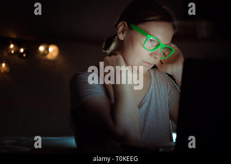 Woman suffering from severe neck pain while working on laptop computer late at night in her home office Stock Photo