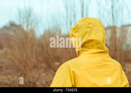 Rear view of woman in raincoat looking into distance on cloudy rainy winter day Stock Photo