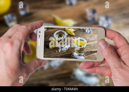 Man taking photo of Mexican traditional alcohol drink Tequila with lemons and salt and ice cube on wood table Stock Photo