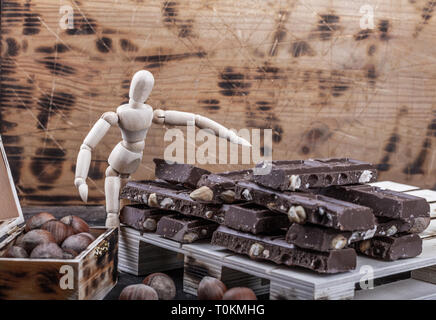 Large amounts of milk chocolate in piles on boards. Hazelnuts in a crate. Stock Photo