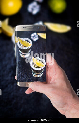 Man taking photo of Mexican traditional  Tequila with lemon, salt and ice cube on dark stone table table Stock Photo