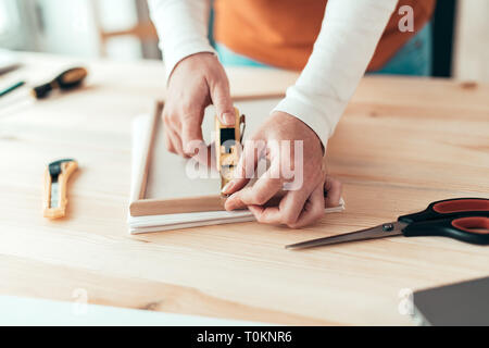 Female carpenter tape measuring picture frame in small business woodwork workshop, close up of hands Stock Photo