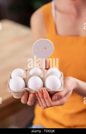 Young lady in bright yellow t-shirt holding bunch of eggs Stock Photo