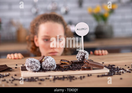 Tired curly-haired woman leaning on kitchen table while touching warning Stock Photo