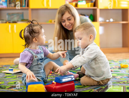 Babysitter plays with babies in nursery or kindergarten Stock Photo