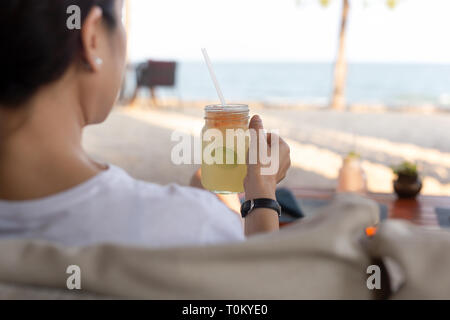 Woman relaxing on the beach with hand glass fresh lemon honey drink. Stock Photo