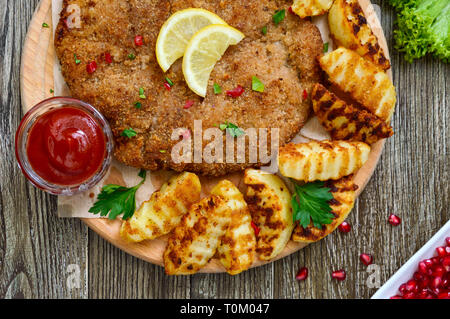 Large schnitzel with baked golden potatoes on a wooden cutting board. Wiener Schnitzel. Top view. Stock Photo